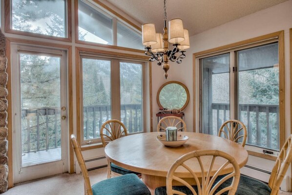 Enjoy meals in this dining area with a round table and four chairs, surrounded by large windows offering views of the surrounding trees.