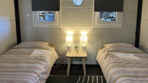 Une chambre avec deux lits, chacun doté de draps à rayures, une petite table avec deux lampes et un luminaire hexagonal au plafond.