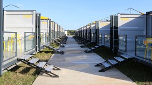 Une rangée de locaux modulaires, semblables à des conteneurs, avec des noms sur les portes, disposés en ligne le long d’un chemin.