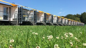 Une rangée de wagons de train, dont les portes sont ouvertes, se trouve au milieu d’un champ d’herbe.