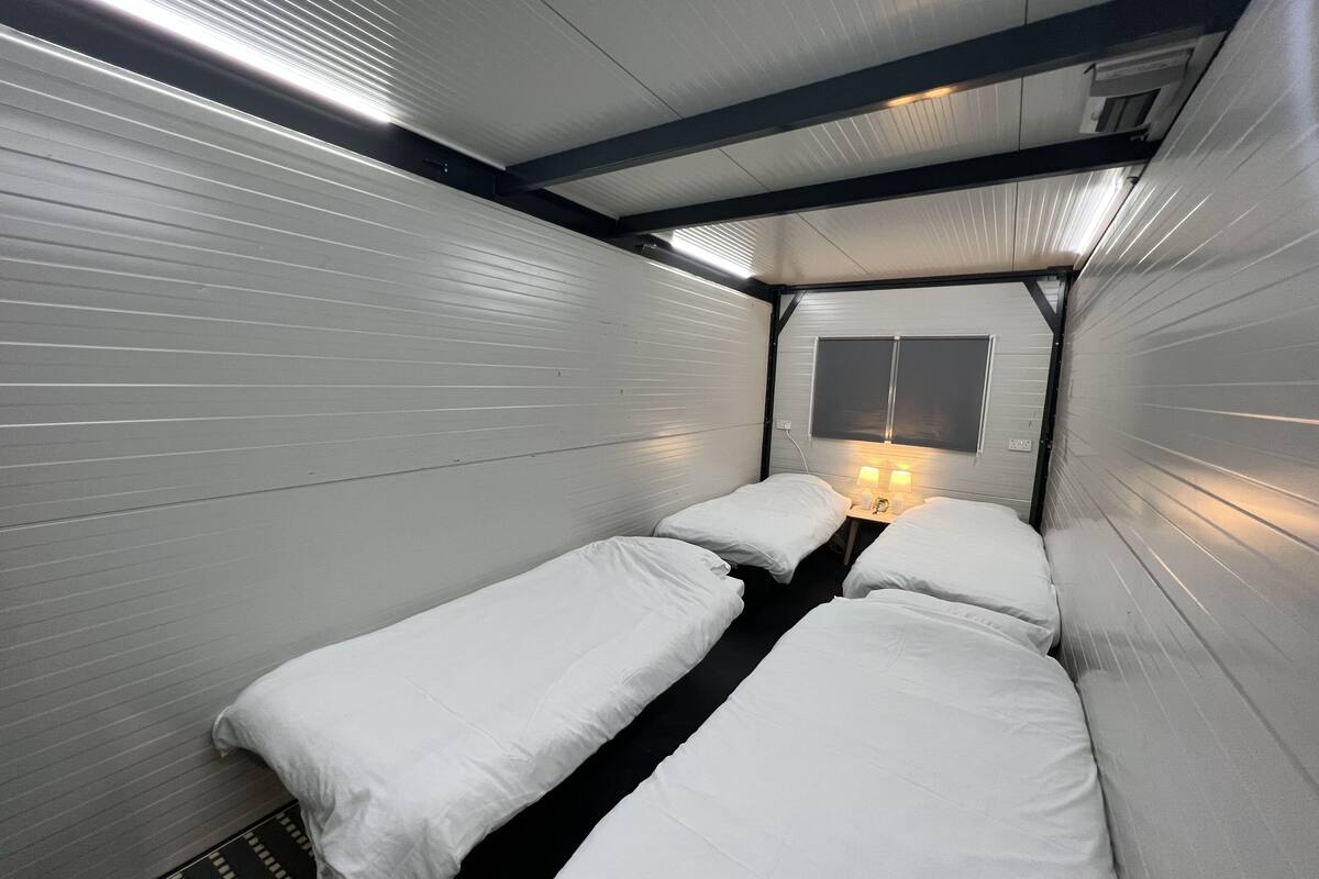 A compact, single-room hotel with two beds, a small table with lamps, and a window with blinds.