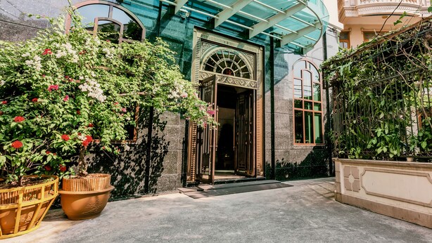 Une cour avec l’entrée d’un bâtiment, des plantes en pot et une structure en verre.