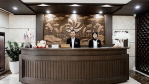 Un comptoir d’accueil avec deux employés, un mur décoré de motifs floraux et une caméra de surveillance.