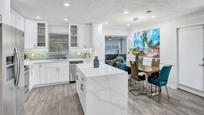 A modern kitchen with white cabinets, a marble island, and a dining area with blue chairs. - By Pier- Heated Pool- 5 Stars! Marbella (Fort Lauderdale)
