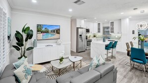 A modern living room with a grey sofa, a coffee table, and a TV displaying a pool scene. - By Pier- Heated Pool- 5 Stars! Marbella (Fort Lauderdale)