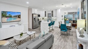A modern living room with a grey sofa, a coffee table, and a TV displaying a pool scene. - By Pier- Heated Pool- 5 Stars! Marbella (Fort Lauderdale)