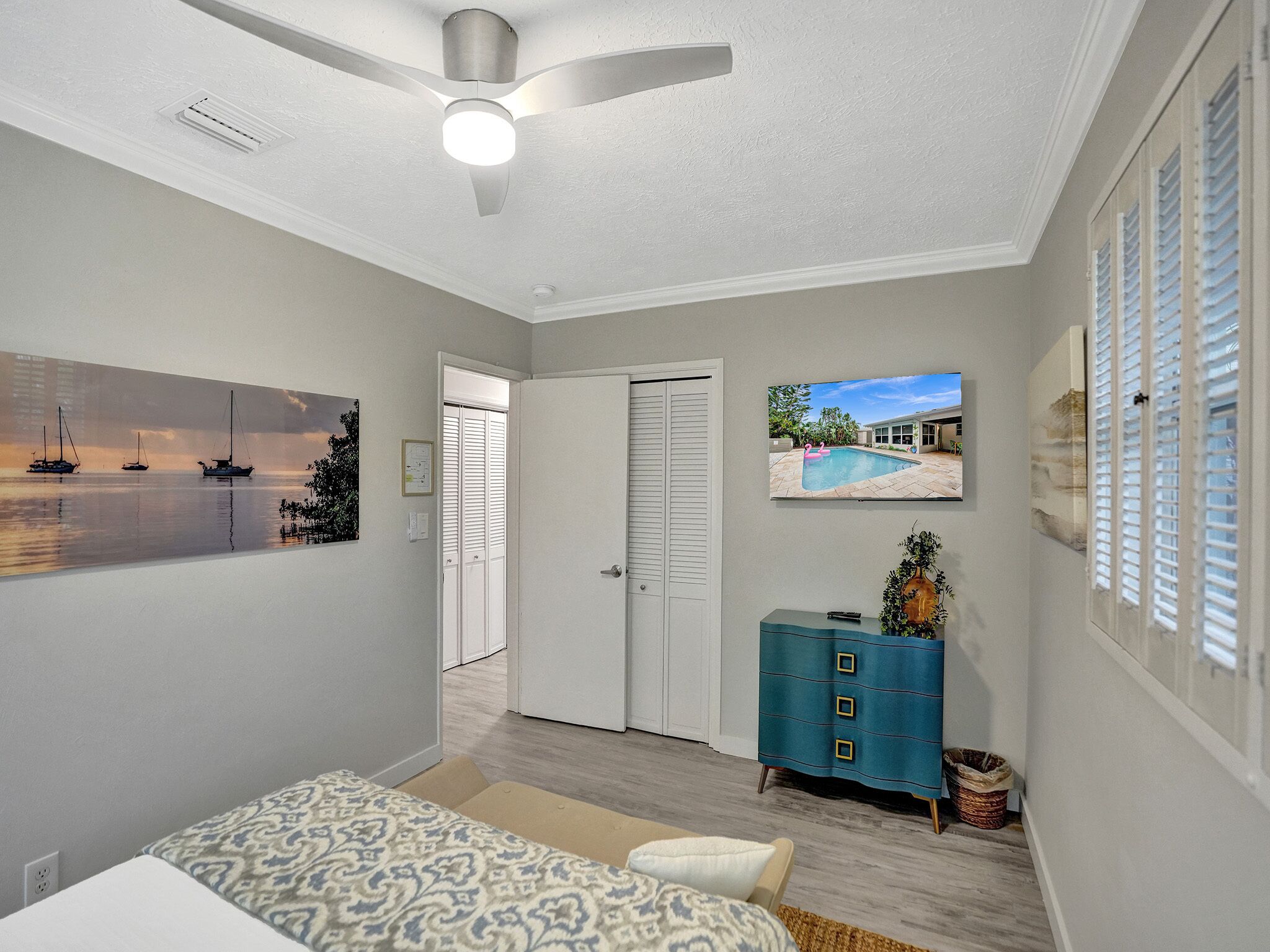 Een slaapkamer met een bed, een plafondventilator, een dressoir en een schilderij van een strandgezicht.
