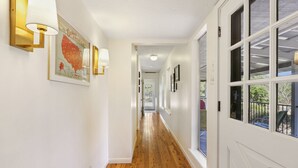Un couloir doté d’un plancher en bois, de murs blancs et d’une porte comportant plusieurs fenêtres.