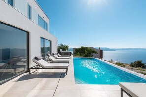 A modern poolside area with lounge chairs and a clear view of the sea.