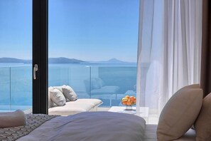 A modern hotel room with a large glass balcony, a bed, a sofa, and a small table with fruit. - Villa Ultima with sea view, private pool&jacuzzi (Ripenda Kosi)