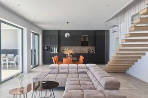 A modern living room with a sectional sofa, a dining table with chairs, and a staircase with wooden steps. - Villa Ultima with sea view, private pool&jacuzzi (Ripenda Kosi)