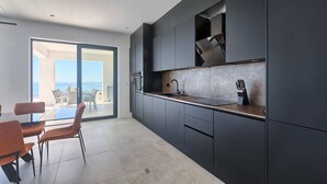 A modern kitchen with dark cabinetry, a countertop, and a sink. There is a dining area with orange chairs and a table. - Villa Ultima with sea view, private pool&jacuzzi (Ripenda Kosi)