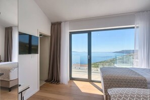 Una habitación de hotel moderna con un amplio ventanal corredero al mar, una cama y un televisor.
