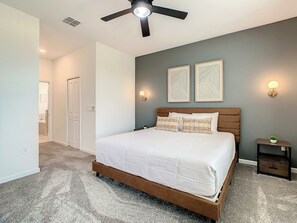 A bedroom with a bed, a ceiling fan, two wall-mounted lights, and a nightstand with a plant.