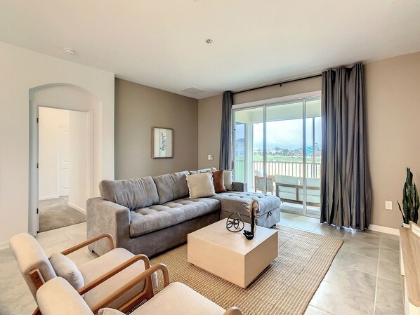 A modern living room with a grey sofa, a wooden coffee table, and a view of a balcony.