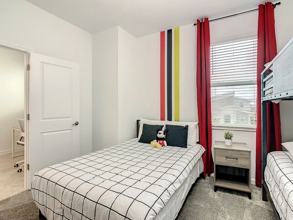 A bedroom with a bed, a nightstand, a window with blinds, and a door.
