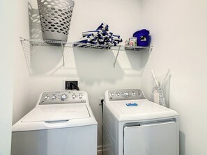 A laundry area with two washing machines and shelves above containing cleaning supplies.