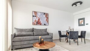Ett modernt vardagsrum med en grå soffa, ett runt soffbord i trä och en matplats med ett bord i glas och svarta stolar.