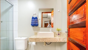 A bathroom with a white toilet, a sink with a mirror above it, and a wooden door. - POUSADA MARIA DO LAMPIÃO  (Jijoca de Jericoacoara)