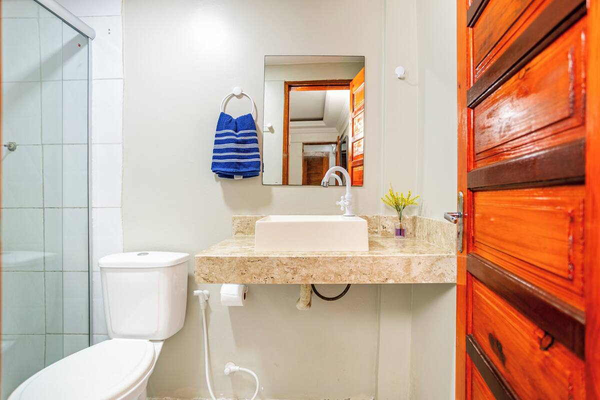 Une salle de bain avec des toilettes blanches, un lavabo avec un miroir au-dessus et une porte en bois.