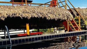 A pool area with a thatched roof structure, a ladder, and a small platform with seating. - POUSADA MARIA DO LAMPIÃO  (Jijoca de Jericoacoara)