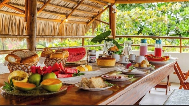 A breakfast buffet with various foods and drinks, including bread, pastries, fruits, and a coffee station. - POUSADA MARIA DO LAMPIÃO  (Jijoca de Jericoacoara)