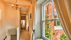 A narrow hallway with a window overlooking a brick wall and greenery. A white radiator and a blue patterned bench are visible.