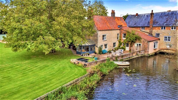A riverside property with a conservatory, a boat dock, and a well-maintained lawn.