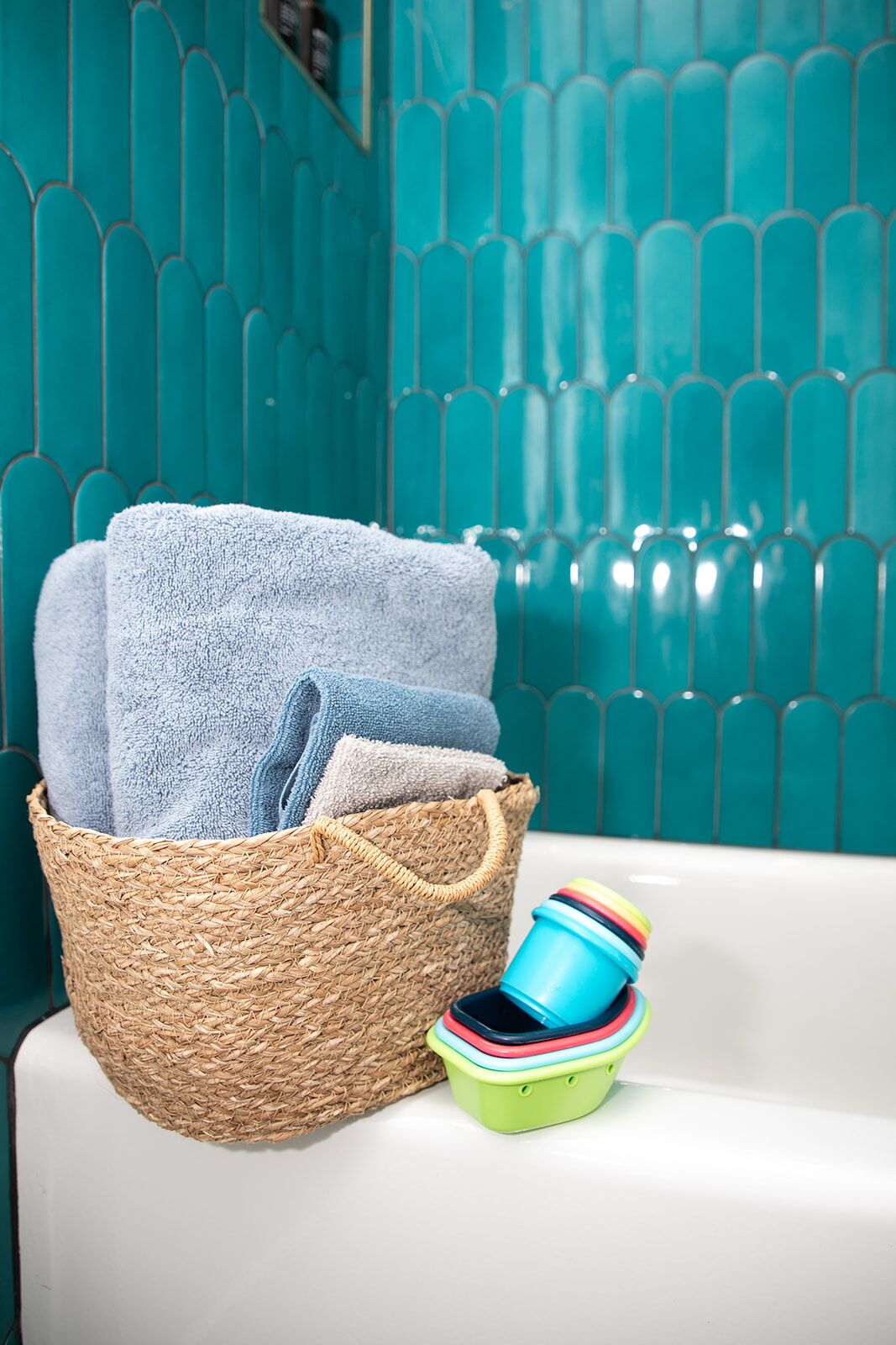 Ein Badezimmer mit einem gewebten Korb, der gefaltete Handtücher und farbenfrohe Behälter enthält, sowie einer weißen Badewanne.