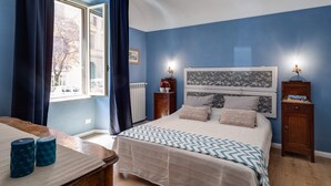 A bedroom with a bed, two bedside tables, a window with curtains, and a view of the outside. - femasuites (Rome)