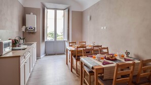 A modern kitchen with a built-in microwave, a water heater, and a dining area with wooden chairs and a table set for breakfast. - femasuites (Rome)