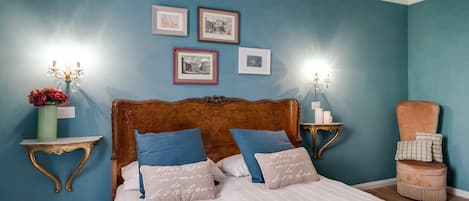A bedroom with a bed, bedside tables, a nightstand, a chair, and wall-mounted pictures.