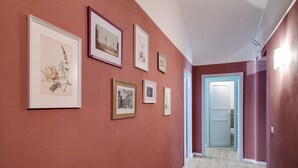 A hallway with framed artwork on the walls, a wooden floor, and a door at the end. - femasuites (Rome)
