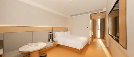 Una habitación de hotel moderna con una cama grande, una mesa redonda, un cubo de basura pequeño y un ventanal amplio.