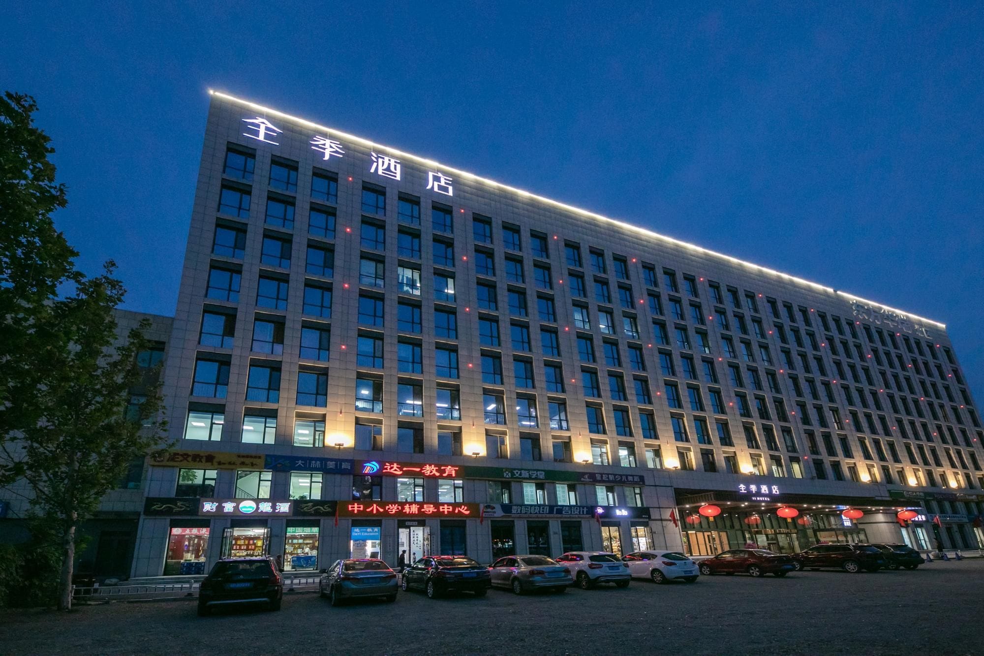 A multi-story hotel building with illuminated signage and a parking lot in front.