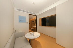 A modern hotel room with a round marble table, a sofa, a large window, and a wall-mounted artwork. - Ji Hotel (Beijing)