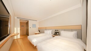 Habitación de hotel con dos camas, una mesita de noche con teléfono y lámpara, una pequeña mesa redonda con una silla y un ventanal grande.