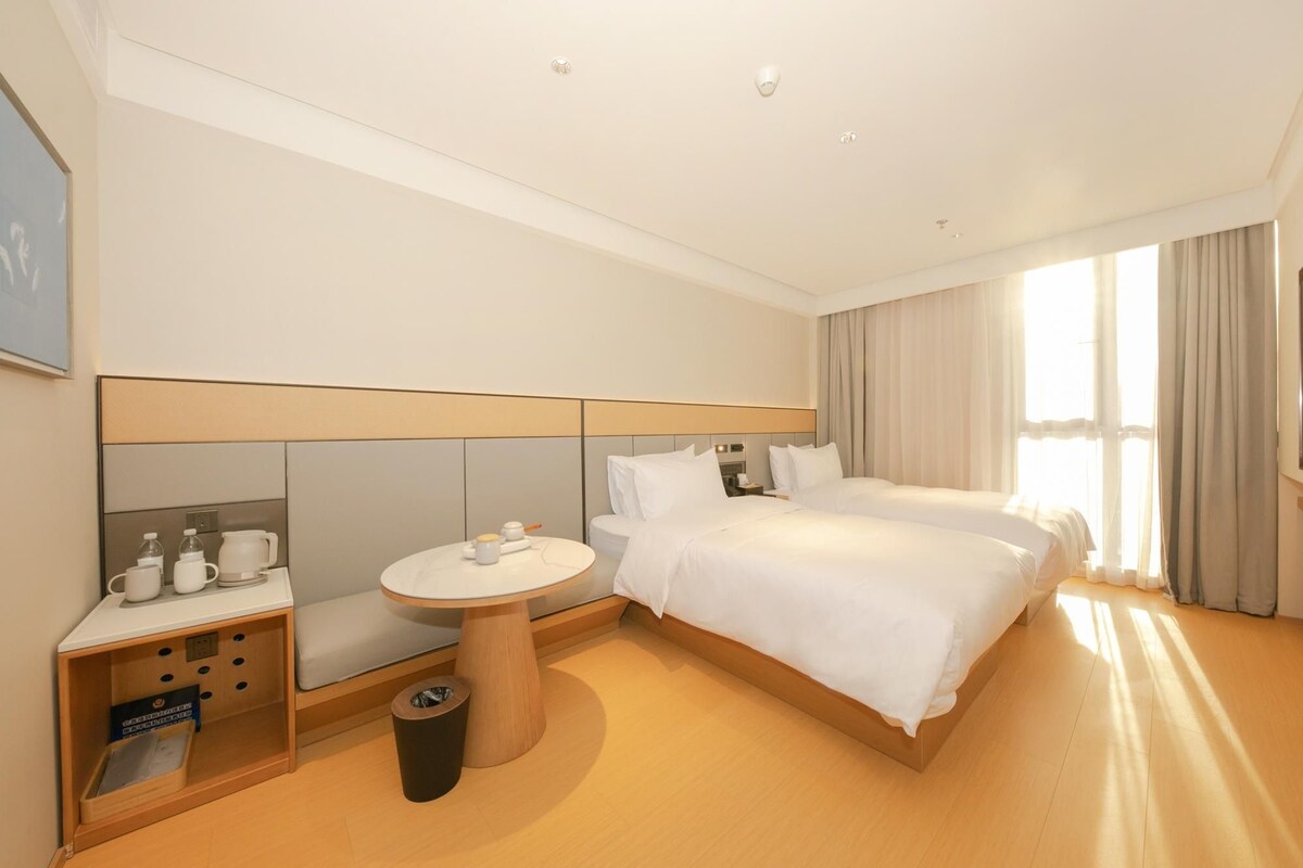 A hotel room with a large bed, a small round table with a chair, a sofa, and a trash bin.