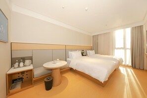 A hotel room with a large bed, a round table with a chair, a small seating area with a bench, and a trash bin. - Ji Hotel (Beijing)
