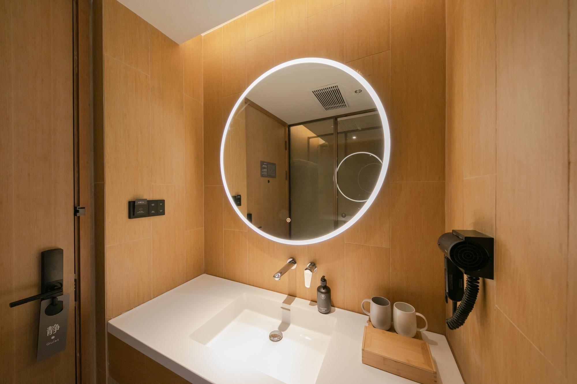 Un baño moderno con un espejo redondo, un lavabo y un secador de pelo montado en la pared.