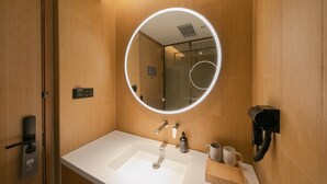 A modern bathroom with a round mirror, a sink, and a hairdryer mounted on the wall. - Ji Hotel (Beijing)