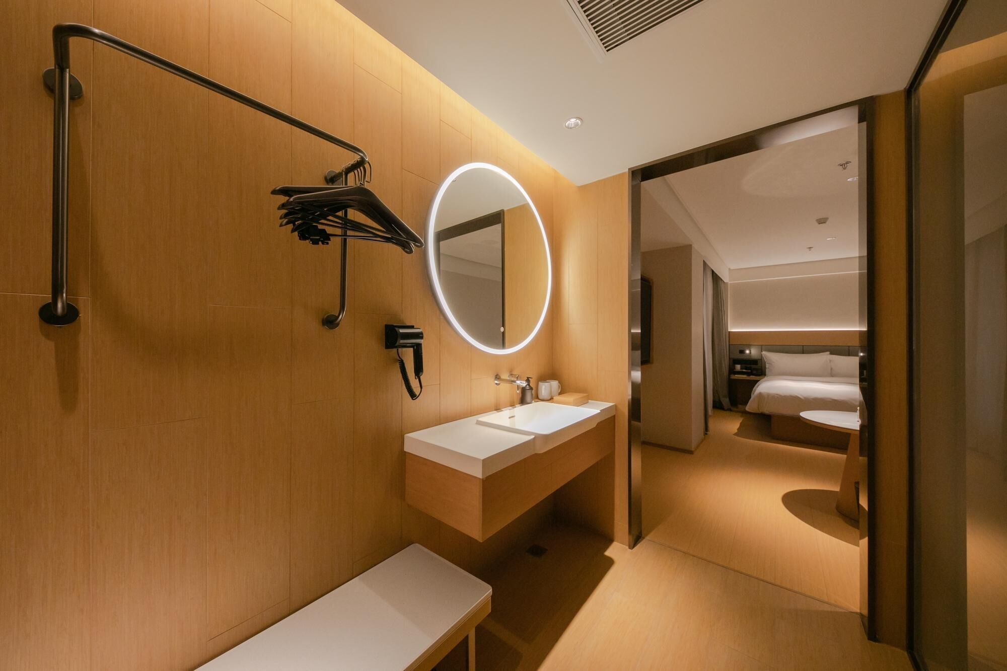 Ein modernes Badezimmer mit einem Holzbadschränkchen, einem runden Spiegel mit Beleuchtung und einer Duschkabine.