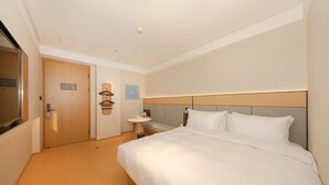 Habitación de hotel con una cama grande, una mesita de noche, una pequeña mesa redonda, un espejo y una puerta.