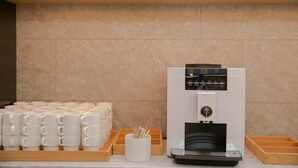 A coffee machine with a digital display, a stack of white mugs, and a tray of wooden boxes. - Ji Hotel (Beijing)