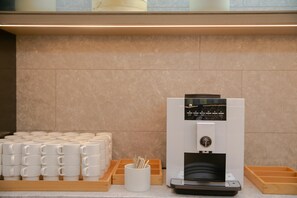 En kaffemaskine med digitalt display, en stabel hvide krus og en bakke med trææsker.