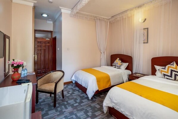 A hotel room with two beds, a desk, a chair, and a door.