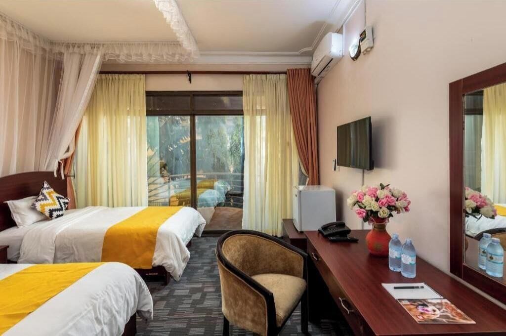 A hotel room with two beds, a desk, a chair, a TV, and a window with curtains.