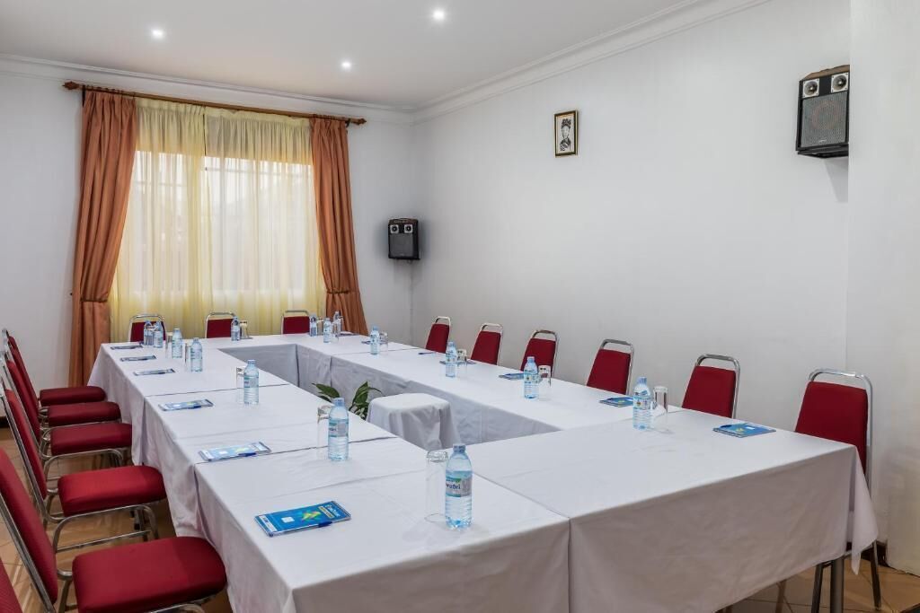 A conference room with a long table, red chairs, water bottles, and a speaker on the wall.