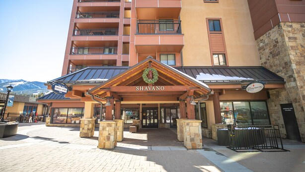 Un hotel de varios pisos con una entrada destacada, un cartel que dice 'Shavano' y fachada de piedra.