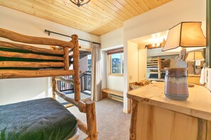 Una panca di legno con seduta imbottita, un tavolo in legno con una lampada e vista su un balcone con ringhiera.